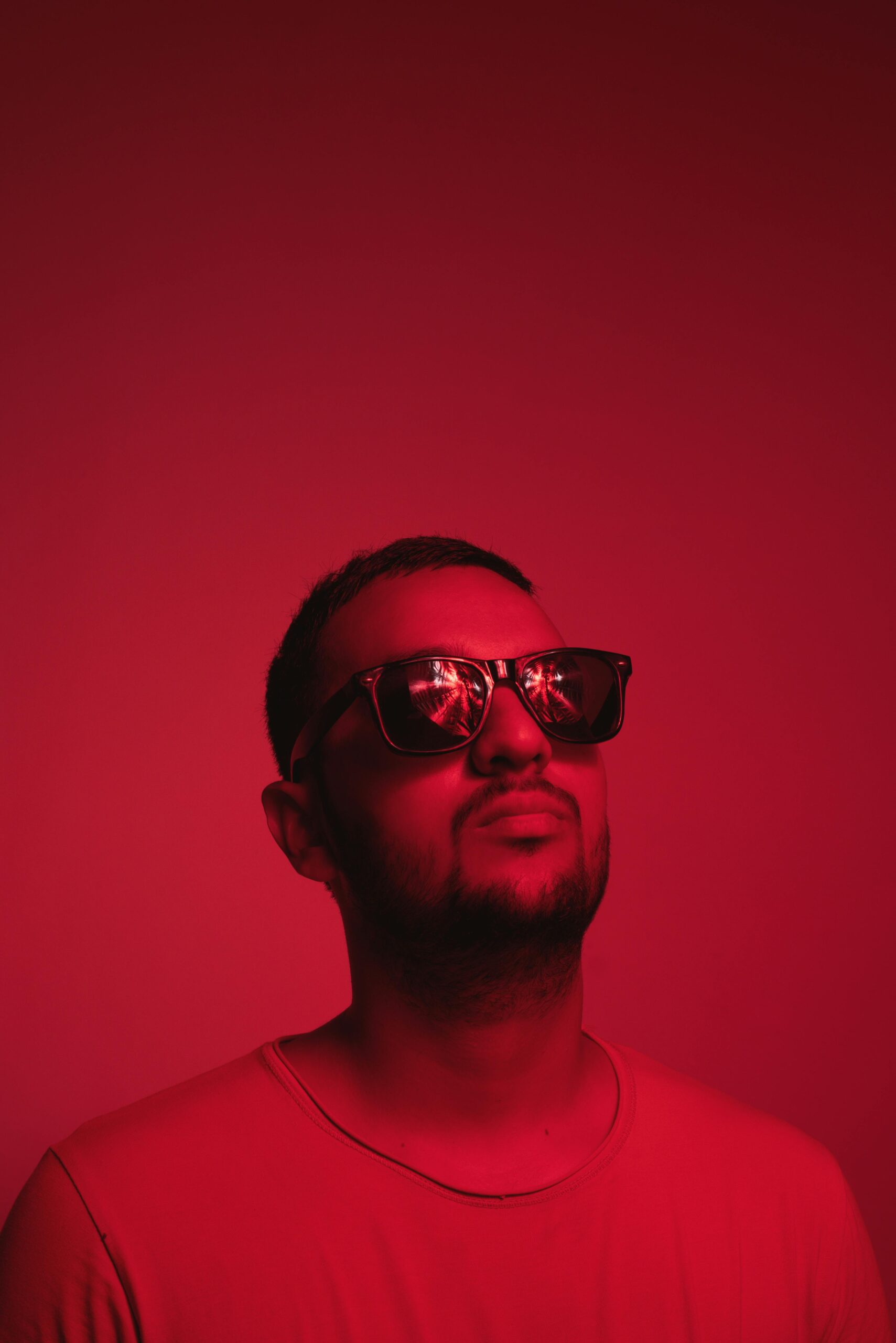 Stylish portrait of a young man wearing sunglasses against a red background, showcasing modern fashion.